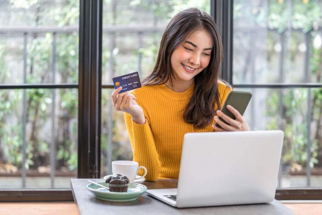 Young female holds credit card in hand while looking at phone